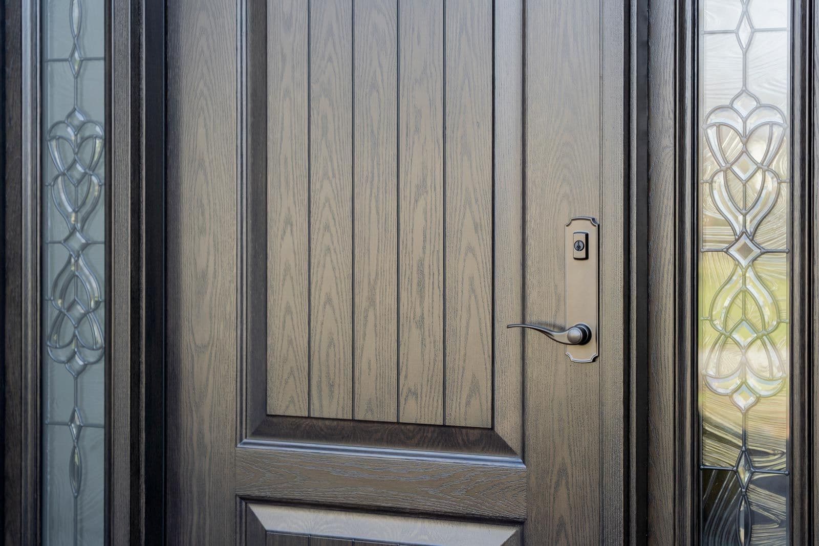 Close-up of an elegant dark wood front door with vertical panels, ornate stained-glass sidelights, and a modern metal handle and lock.