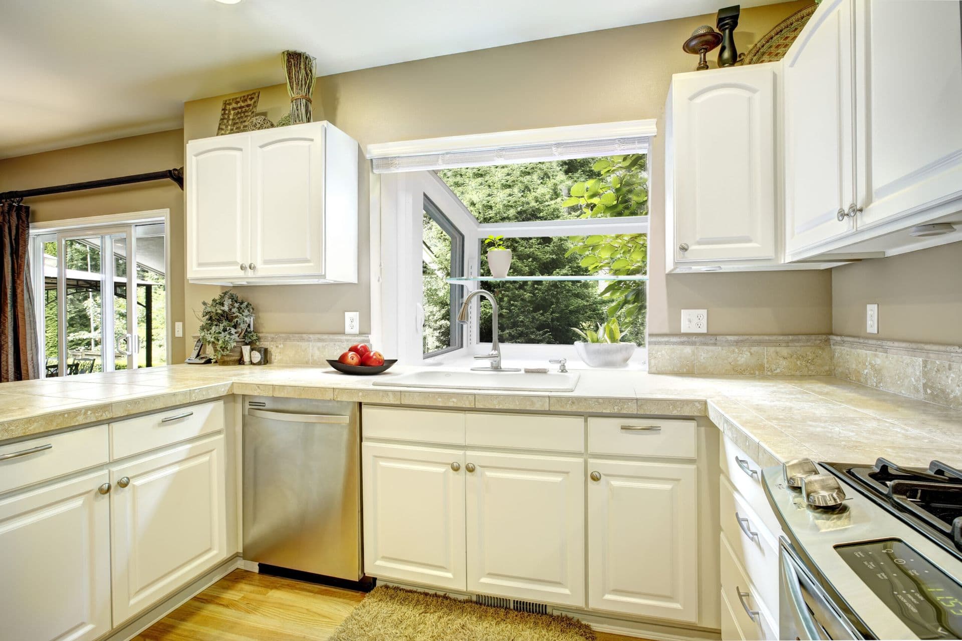 Bright, inviting kitchen with white cabinets, granite counters, sink beneath an open window, stainless dishwasher, and gas stove.