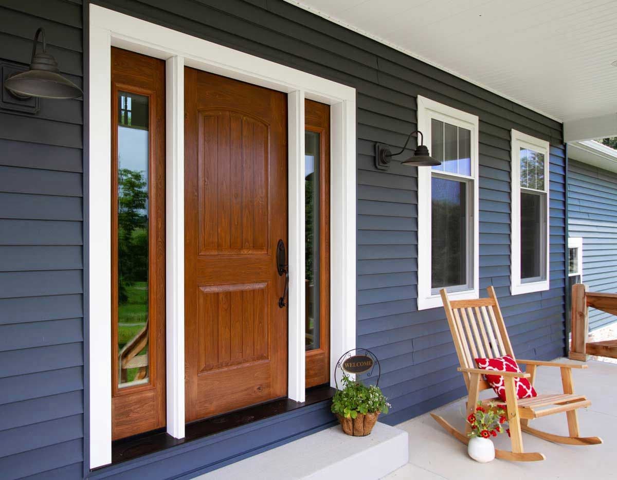 Inviting front porch with navy siding, a warm wooden door, rocking chairs, bright windows, and potted flowers creating a welcoming mood.